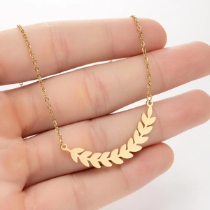 Close-up of a delicate gold wheat leaf pendant necklace resting on a person's hand
