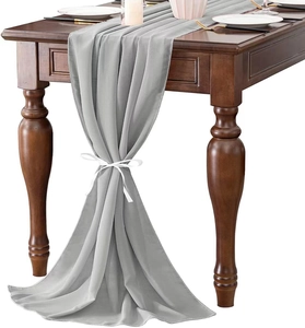 Light gray chiffon table runner on dark wood table with white ribbons for decoration
