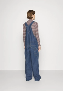 Back view of loose fit denim overalls for women featuring dual rear pockets and strap hooks
