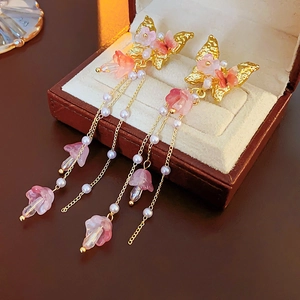 Detail von goldenen Schmetterlings- und rosa Blumen-Kristallquasten-Ohrringen