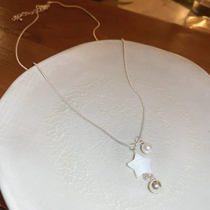 Detail of silver snake chain necklace with white shell star and pearl on ceramic plate