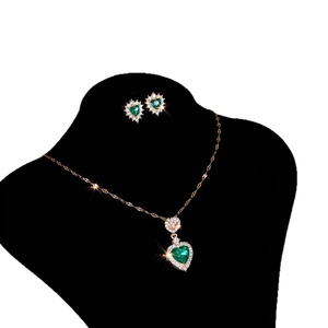 Elegant gold jewelry set with emerald green heart crystals on black velvet display stand