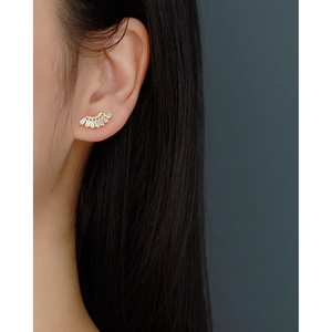 Close-up of a gold fan-shaped stud earring with baguette crystals on a model's ear