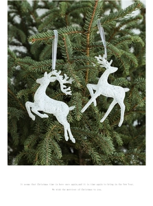 Nahaufnahme von weißen Glitzer-Rentier-Anhängern mit Bändern an einem grünen Weihnachtsbaum