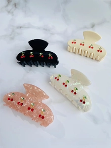 Detail of four acetate claw clips featuring red rhinestone cherry designs in various colors