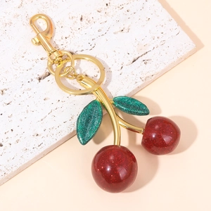 Macro view of cherry keychain with red glitter fruit, green leaves and gold clasp