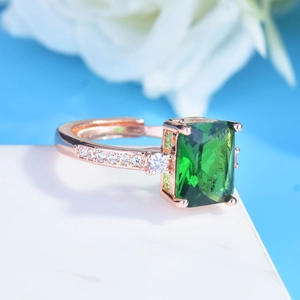 Macro detail of emerald-cut green gemstone ring with rose gold plating and side stones