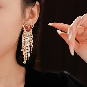 Detail of heart-shaped drop earrings with red crystals and cascading rhinestone tassels