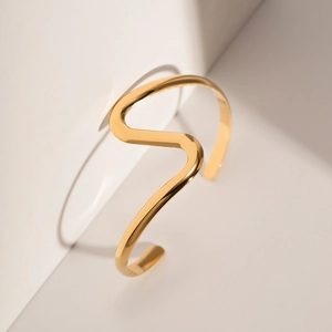 Detailed macro shot of 18K gold plated curved wave bangle on minimalist geometric props