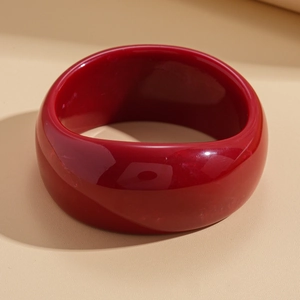 Close-up of a wide chunky red acrylic bangle with a glossy mirror finish and smooth round edges