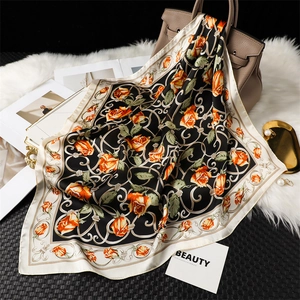 Détail d'un carré de soie avec imprimé floral orange noué sur un sac à main en cuir