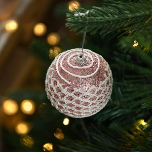 Close-up of pink glitter Christmas ball with white grid pattern on a green tree branch