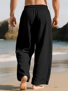 Rear view of black linen casual pants for men featuring elastic waist on a beach background