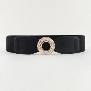 Close-up of a black elastic waist belt featuring a round gold buckle with sparkling rhinestones