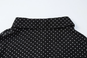 Dettaglio ravvicinato del colletto a polo e del tessuto in chiffon nero a pois dell'abito