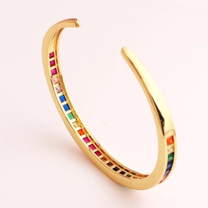 Detail van een gouden C-vormige open armband met een regenboog aan pave-gezette zirkonia's