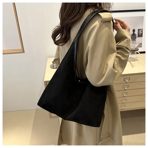 Detail of a large black suede shoulder bag worn by a model in a cozy indoor setting