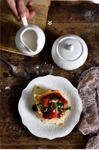 Close-up of embossed ceramic cream pitcher, sugar bowl, and plate on dark wood surface