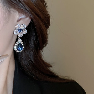 Detail of silver flower earrings with blue teardrop zircon and white crystal inlays