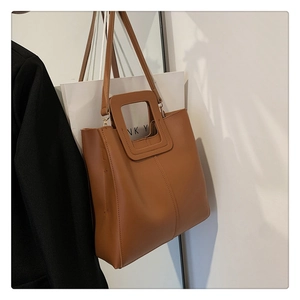Dettaglio di una borsa tote marrone in pelle sintetica appesa su una parete bianca