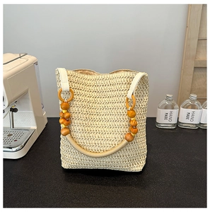 Beige woven straw tote bag with beaded handle displayed on a black countertop