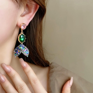 Détail de boucles d'oreilles vintage en or avec pierres roses, vertes et queues de sirène