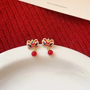Close-up of red Chinese lion dance earrings with tassel beads on a white ceramic dish