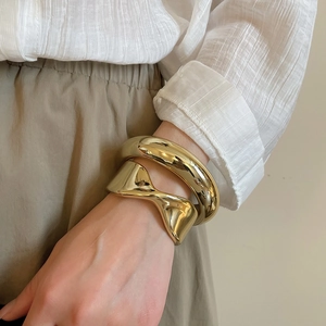 Detail of chunky gold bracelets set with polished finish and unique geometric twisted design