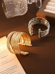 Macro shot of layered wavy C-shaped cuffs in gold and silver finish on a luxury setup