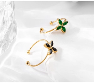 Close-up of gold clover ring with green and black marquise gemstones on white fabric