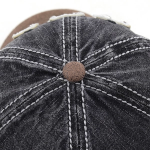 Macro detail of washed black denim baseball cap with brown top button and white stitching