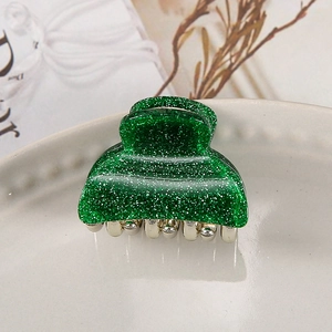 Close-up of a sparkling green Christmas acrylic hair clip on a white ceramic plate