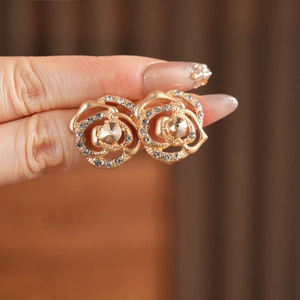 Detailed close-up of golden rose earrings featuring small crystals and matte metal texture