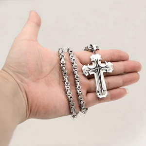 Close-up of a hand holding a double-layered silver stainless steel cross pendant necklace