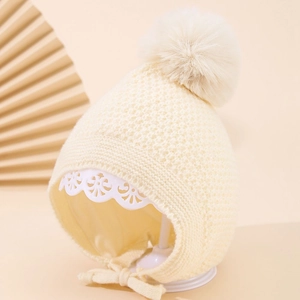 Detail der Strickstruktur und Bommel an cremefarbener Baby-Strickmütze mit Ohrenklappen
