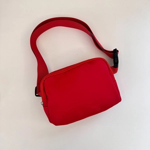 Close-up of red nylon crossbody bag with wide webbing strap and black buckle closure