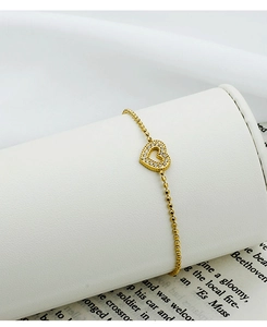 Detail of gold heart charm bracelet with cubic zirconia on white silk and book