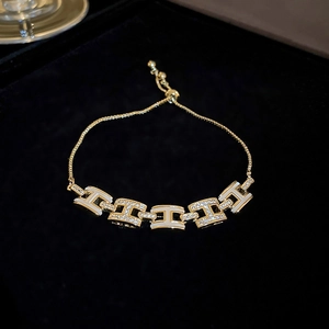 Détail macro du bracelet doré à lettres H avec émail blanc et cristaux étincelants
