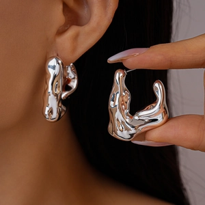 Modern irregular fluid silver hoop earrings featuring a polished molten lava style design