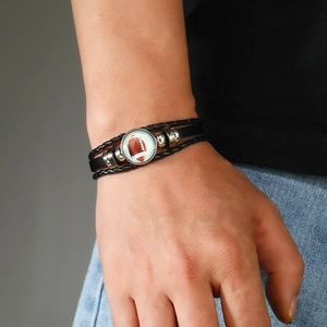 Gros plan d'un bracelet multicouche en cuir noir avec pendentif de football en verre au poignet