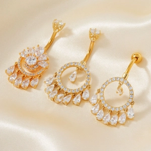 Detaillierte Ansicht von drei goldenen Bauchnabelpiercings mit Zirkonia auf beigem Seidengrund