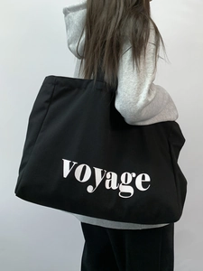 Large black canvas tote bag with white voyage lettering worn by a model in a minimal style