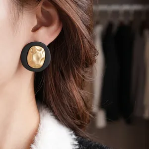 Vintage round matte black and hammered gold earrings shown on a model's ear