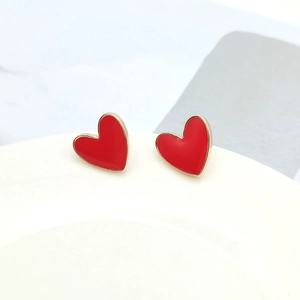 Macro detail of red enamel heart earrings with gold plating on a white ceramic rim