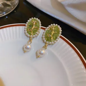 Close-up of rose relief earrings with green resin stone and faux pearl embellishments