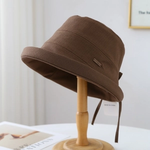 Brown breathable bucket hat with metal tag and tie on minimalist wooden display