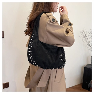 Détail du sac hobo en daim noir avec rivets argentés et décor de cœur sur un manteau kaki
