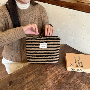 Detail of striped plush cosmetic bag zipper closure and white logo patch in use