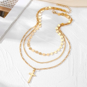Detail of layered gold necklace with polished cross pendant and textured metal chains