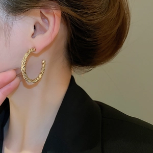 Detail of twisted gold rope hoop earring worn by a model in a minimalist setting